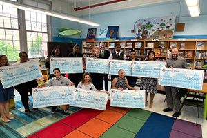 PS 11 staff and guests hold ceremonial grant checks in the school library.