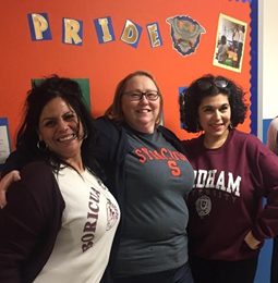 Three educators smiling in front of a Pride bulletin board