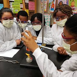 Students in lab coats and safety goggles running a science experiment