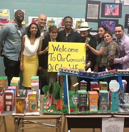 Staff and students with a student-built model city and a Welcome to Our Community sign